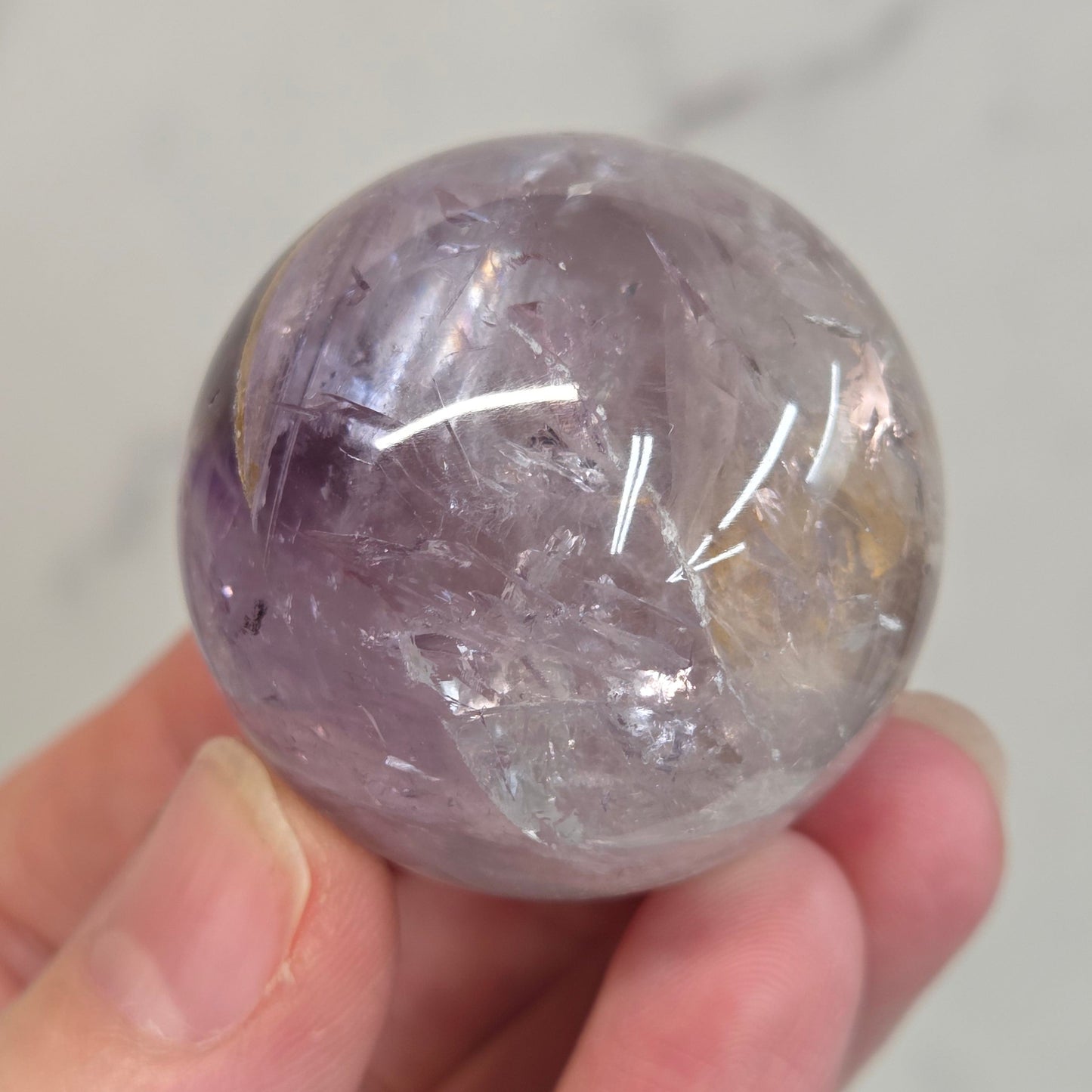 Hand holding a Phantom Amethyst sphere on a white background