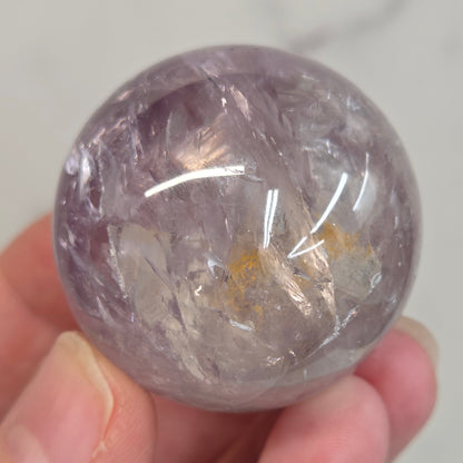 Hand holding a Phantom Amethyst sphere on a white background