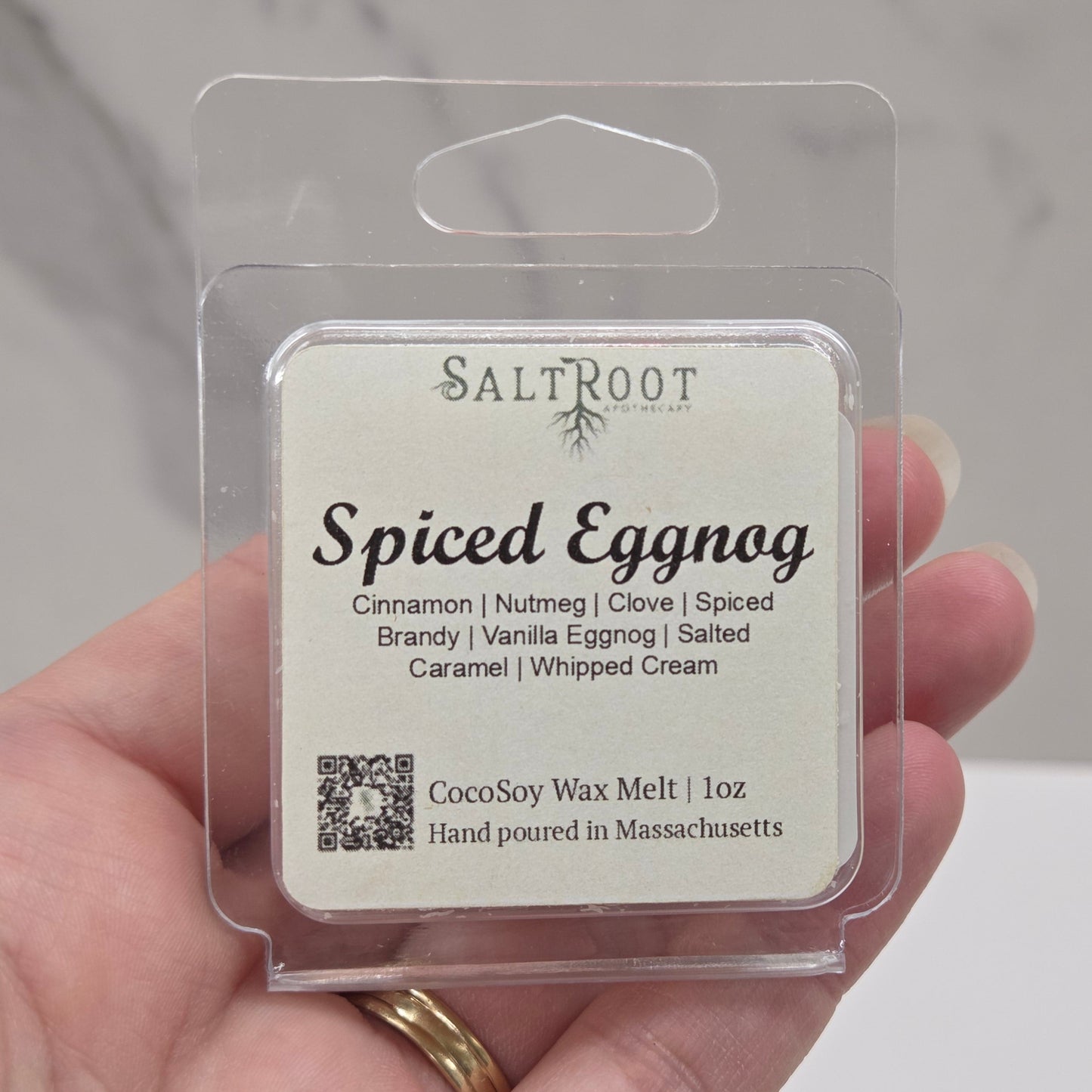 Hand holding a wax melt package labeled 'Spiced Eggnog' by Saltroot against a neutral background.