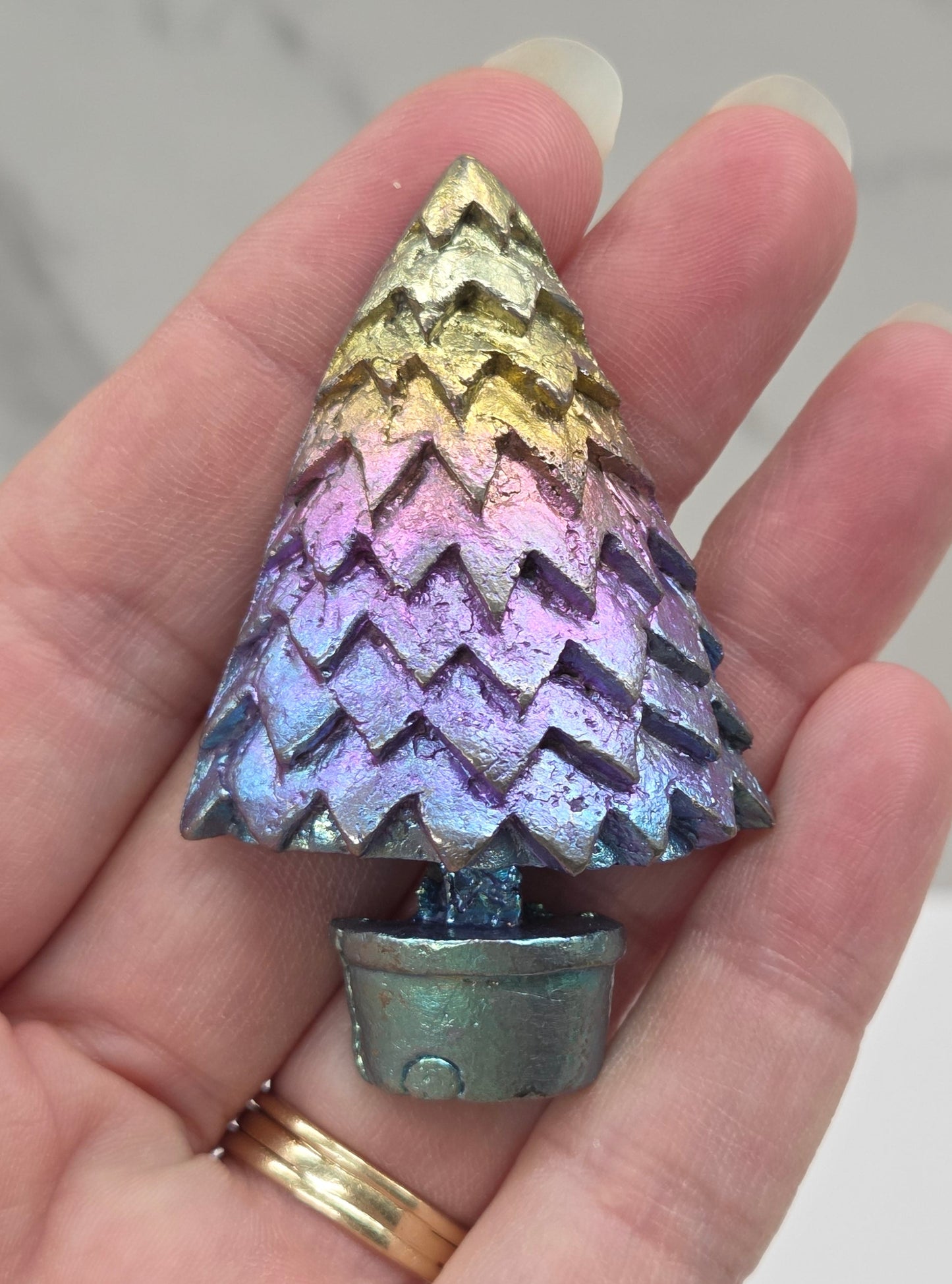 Multicolored, Bismuth tree carving being held in a hand against a neutral background