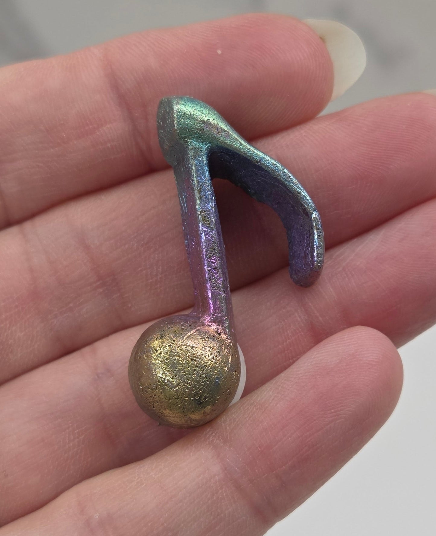 Colorful Bismuth carving shaped like a music symbol held in a hand.