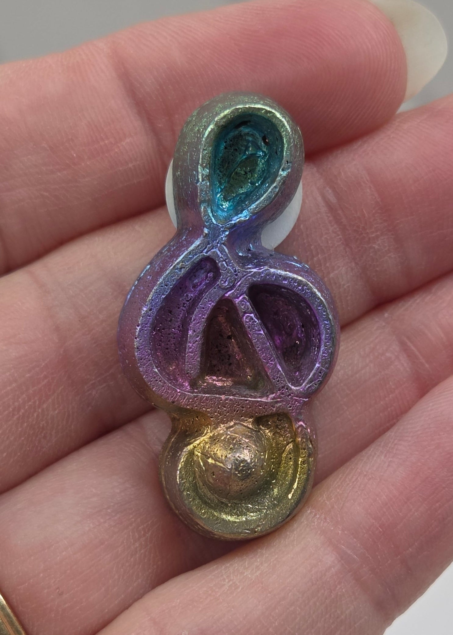 Colorful Bismuth carving shaped like a music symbol held in a hand.
