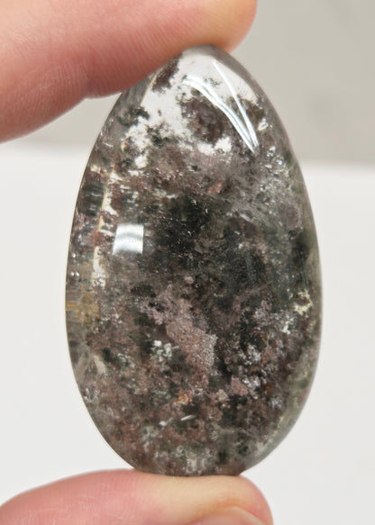 An oval-shaped Garden Quartz pendants displayed on a white surface, varying in color from clear to gray and with different inclinations within the quartz.