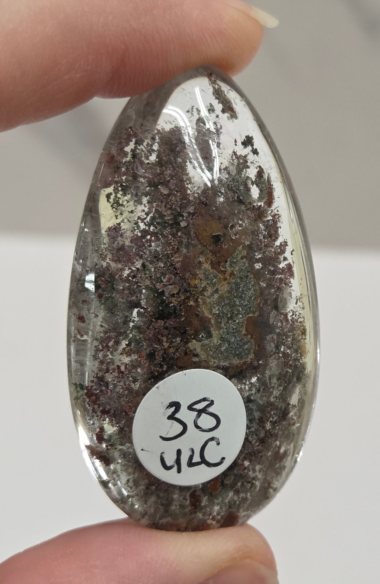 An oval-shaped Garden Quartz pendants displayed on a white surface, varying in color from clear to gray and with different inclinations within the quartz.