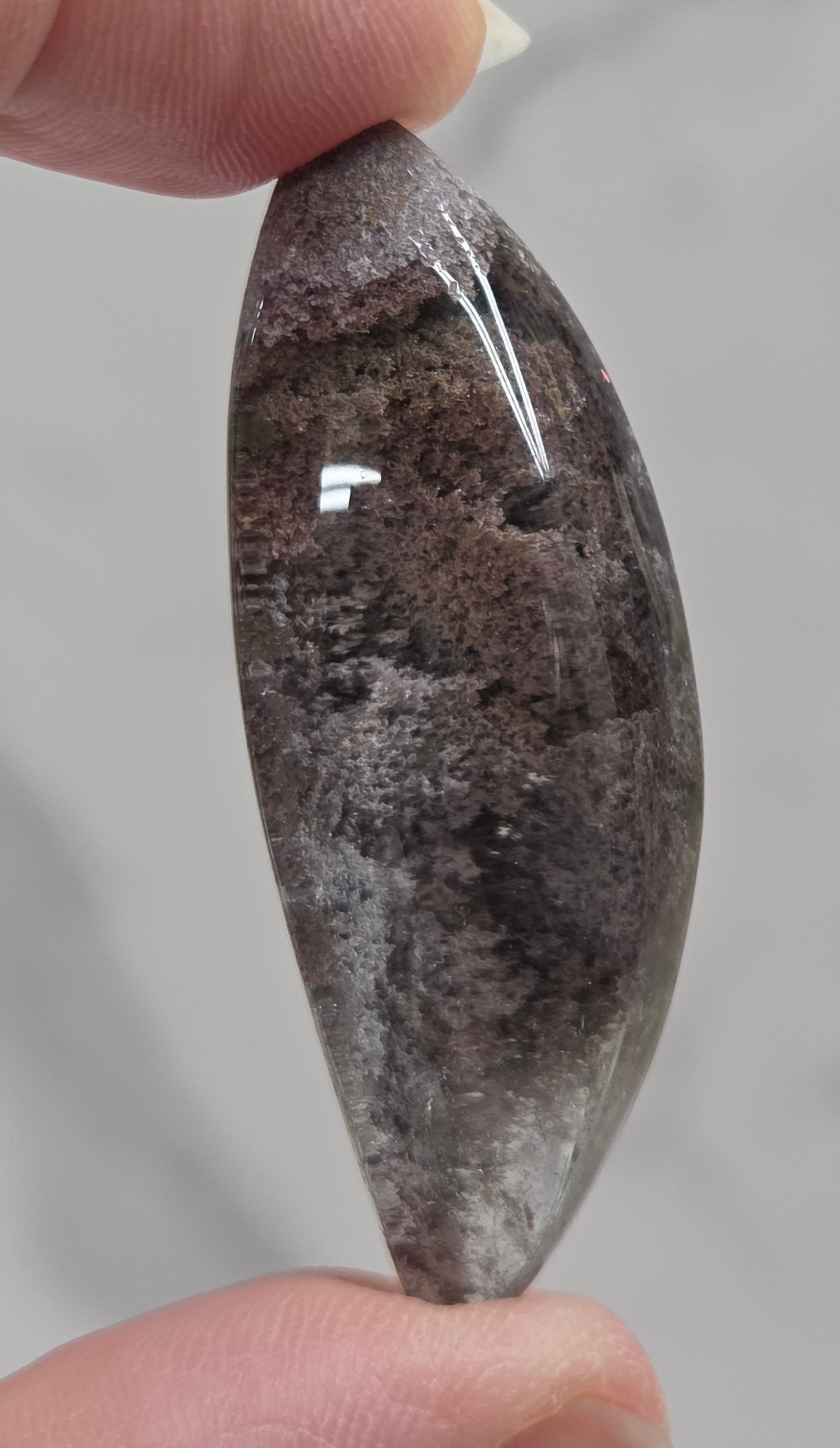 A teardrop-shaped Garden Quartz pendants displayed on a white surface, varying in color from clear to gray and with different inclinations within the quartz.