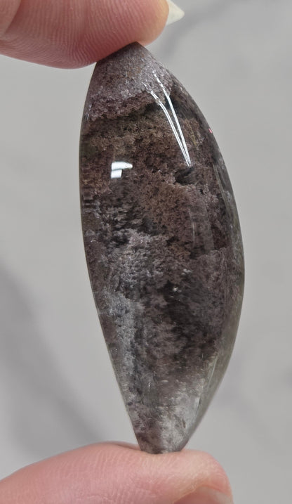 A teardrop-shaped Garden Quartz pendants displayed on a white surface, varying in color from clear to gray and with different inclinations within the quartz.