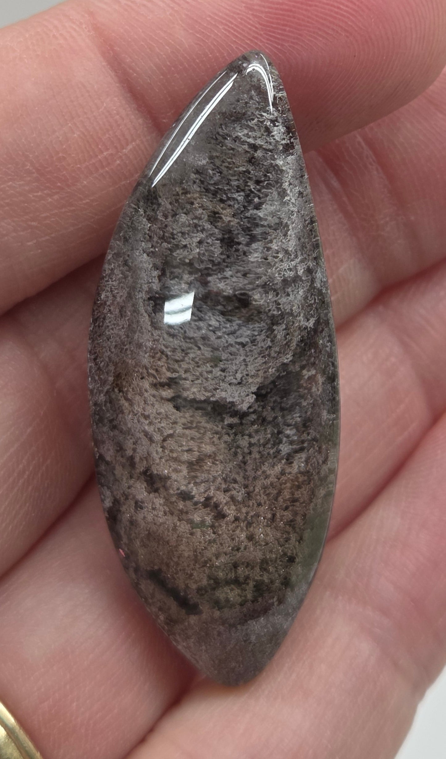 A teardrop-shaped Garden Quartz pendants displayed on a white surface, varying in color from clear to gray and with different inclinations within the quartz.