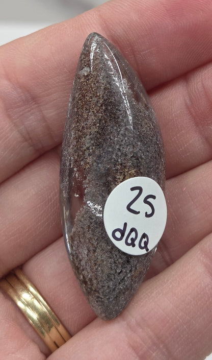 A teardrop-shaped Garden Quartz pendants displayed on a white surface, varying in color from clear to gray and with different inclinations within the quartz.
