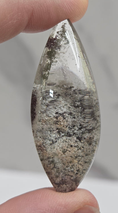 A teardrop-shaped Garden Quartz pendants displayed on a white surface, varying in color from clear to gray and with different inclinations within the quartz.