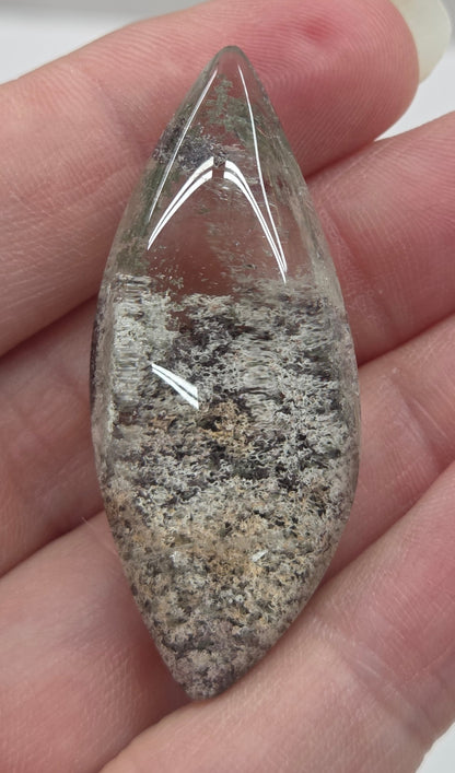 A teardrop-shaped Garden Quartz pendants displayed on a white surface, varying in color from clear to gray and with different inclinations within the quartz.