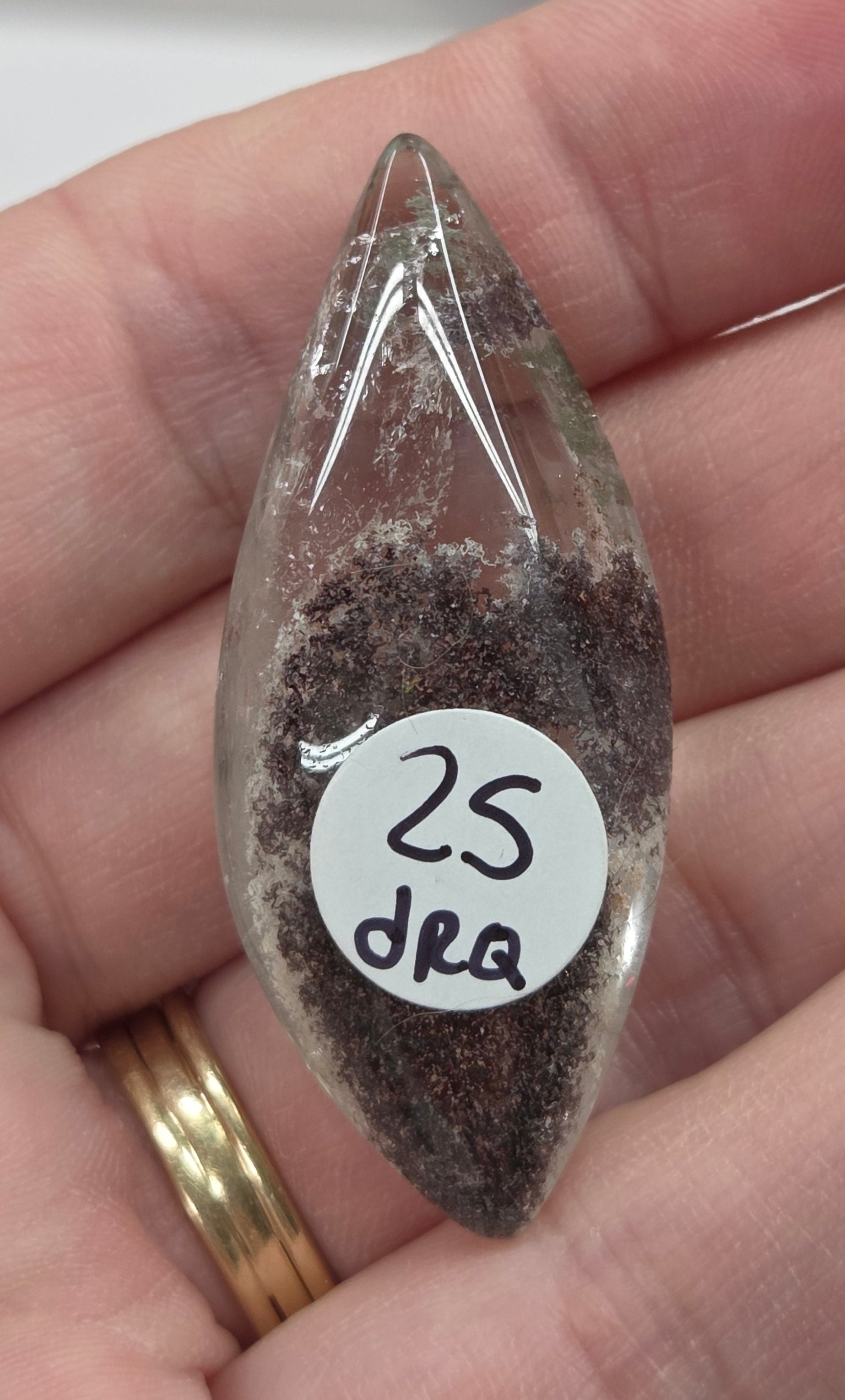 A teardrop-shaped Garden Quartz pendants displayed on a white surface, varying in color from clear to gray and with different inclinations within the quartz.