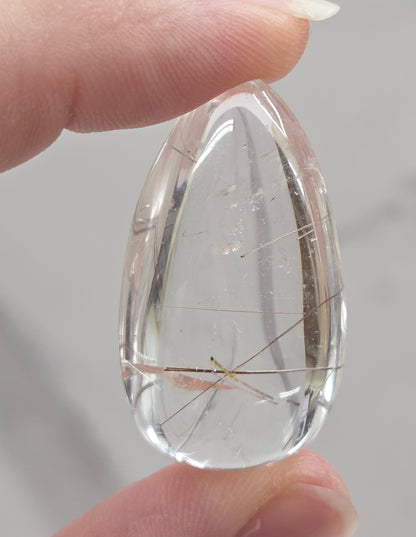 Clear quartz teardrrop shaped crystal with gold rutile inclusions held between fingers