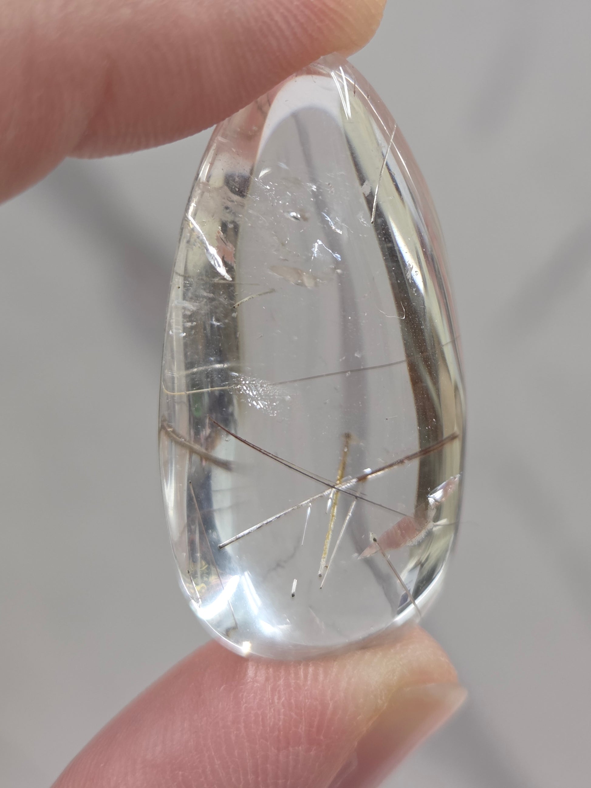 Clear quartz teardrrop shaped crystal with gold rutile inclusions held between fingers