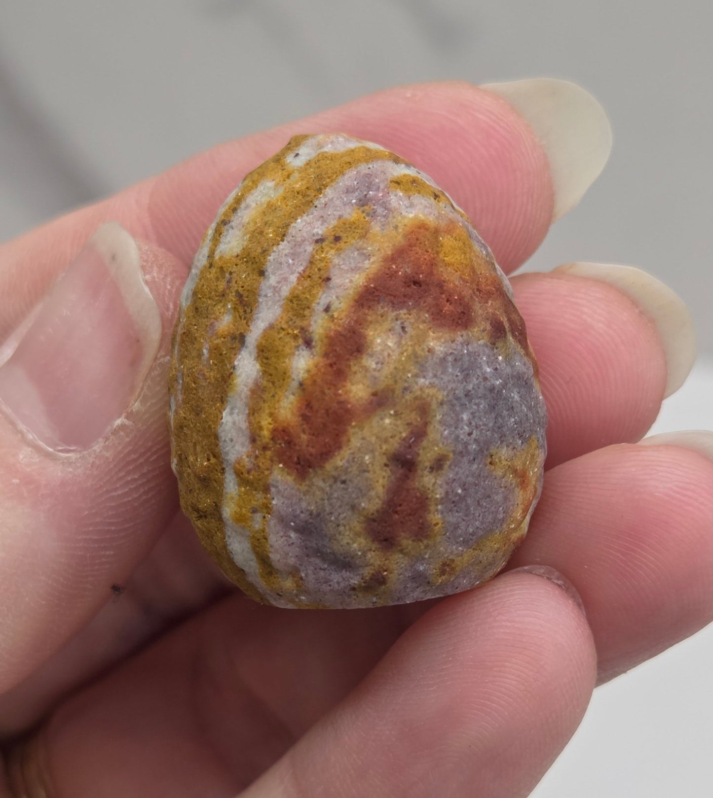 Mookaite polished egg carving with red, yellow and purple patterns on a white background