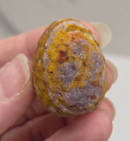 Mookaite polished egg carving with red, yellow and purple patterns on a white background