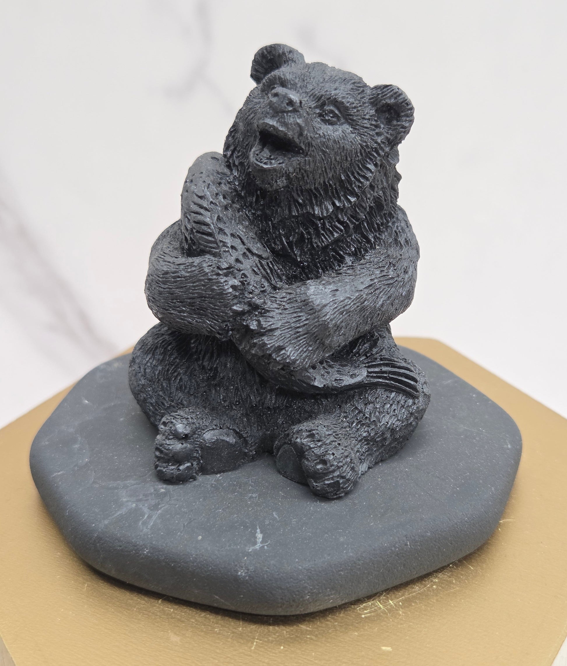 Black bear figurine made of shungite on a gray stone base against a white background
