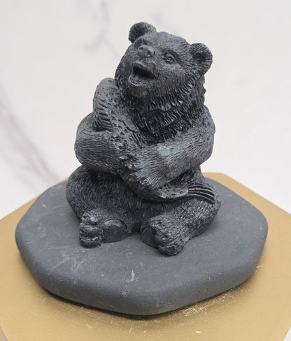Black bear figurine made of shungite on a gray stone base against a white background