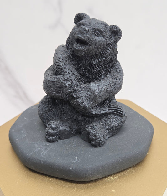 Black bear figurine made of shungite on a gray stone base against a white background