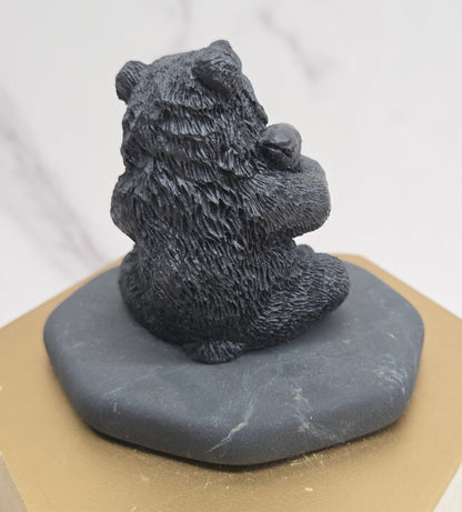 Black bear figurine made of shungite on a gray stone base against a white background