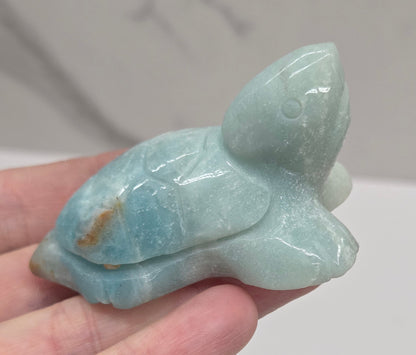 Hand holding a polished Caribbean Calcite crystal in the shape of a sea turtle, with blue and white colors and a light brown pattern.