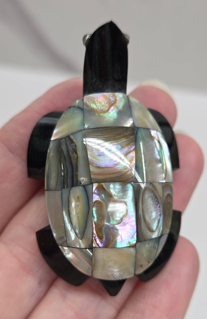 Hand holding a decorative turtle-shaped object with abalone shell  on a plain background