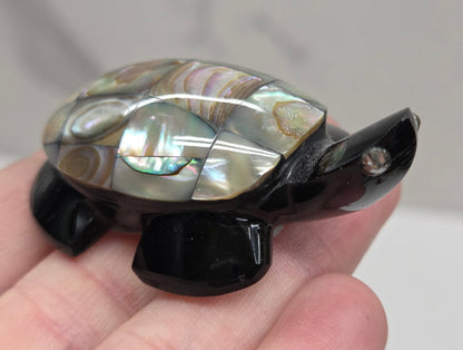 Hand holding a decorative turtle-shaped object with abalone shell  on a plain background