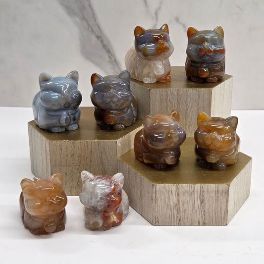 Collection of Agate cat carvings, with varying colors of orange, grey and white, on a wood stand against a white background