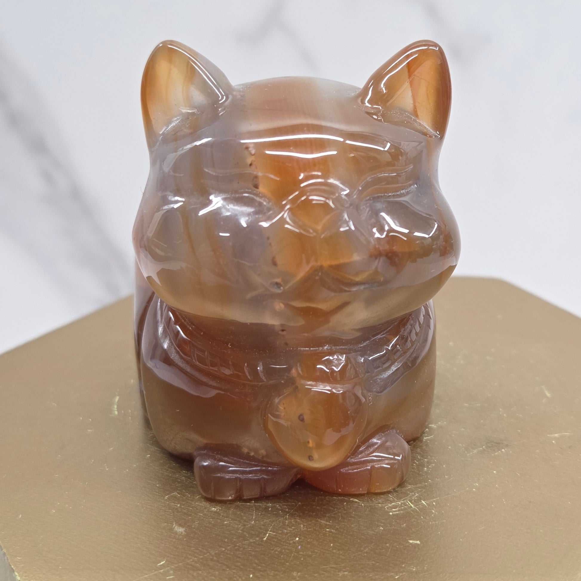 An Agate cat carving, with varying colors of orange, grey and white, on a wood stand against a white background