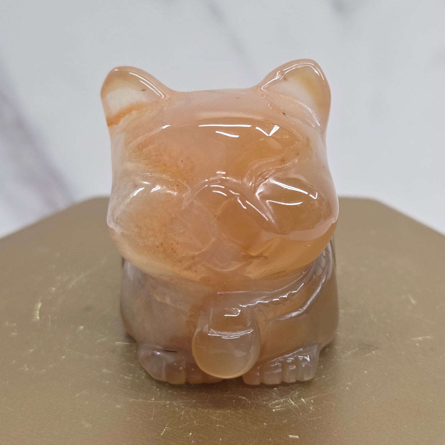 An Agate cat carving, with varying colors of orange, grey and white, on a wood stand against a white background