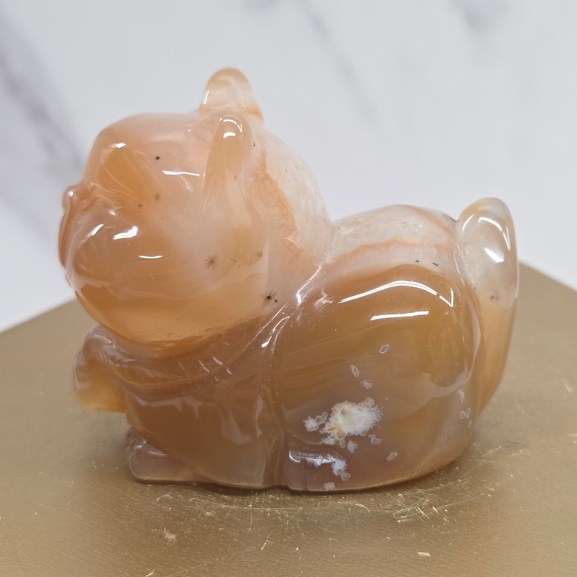 An Agate cat carving, with varying colors of orange, grey and white, on a wood stand against a white background