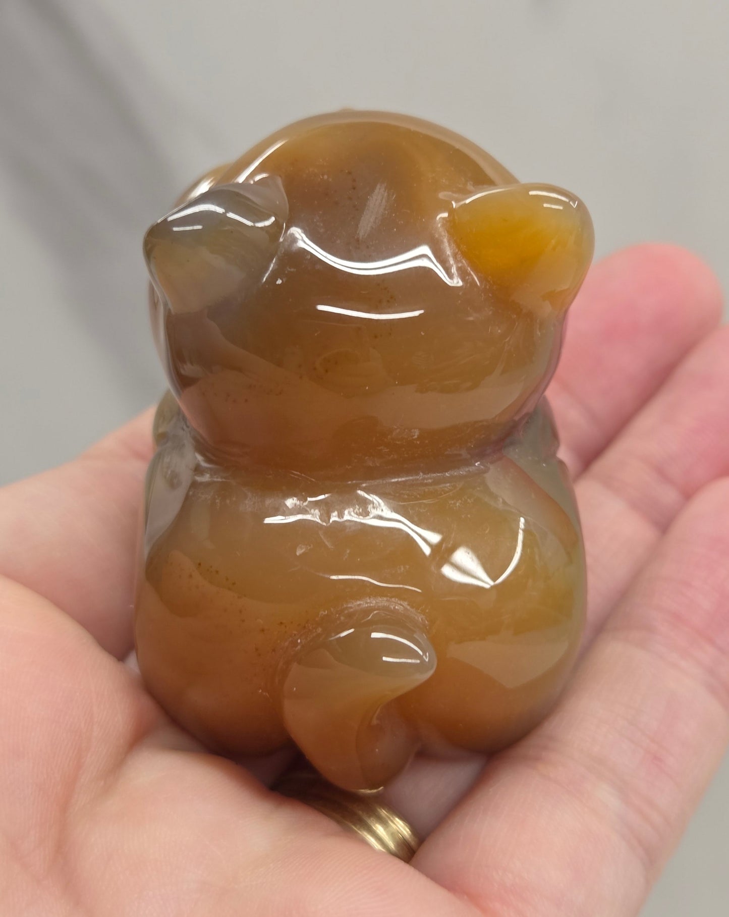 An Agate cat carving, with varying colors of orange, grey and white, being held by a hand against a white background