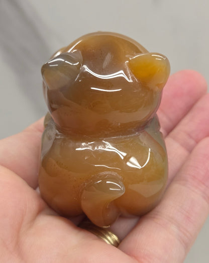 An Agate cat carving, with varying colors of orange, grey and white, being held by a hand against a white background