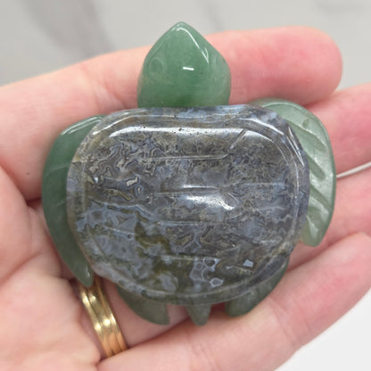 Hand holding a Jade turtle with a Moss Agate shell against a neutral background