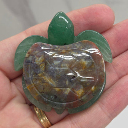 Hand holding a Jade turtle with a Sea Jasper shell against a neutral background