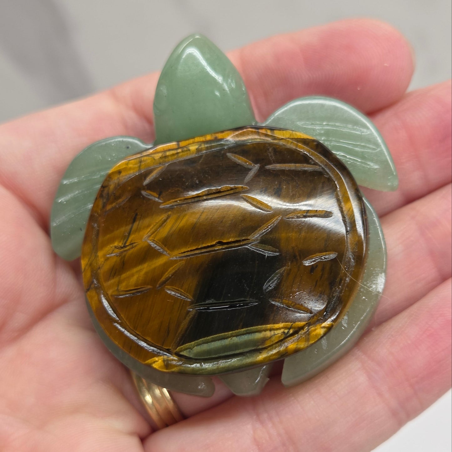 Hand holding a Jade turtle with a Tigers Eye shell against a neutral background