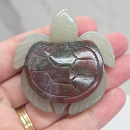 Hand holding a Jade turtle with a Sea Jasper shell against a neutral background