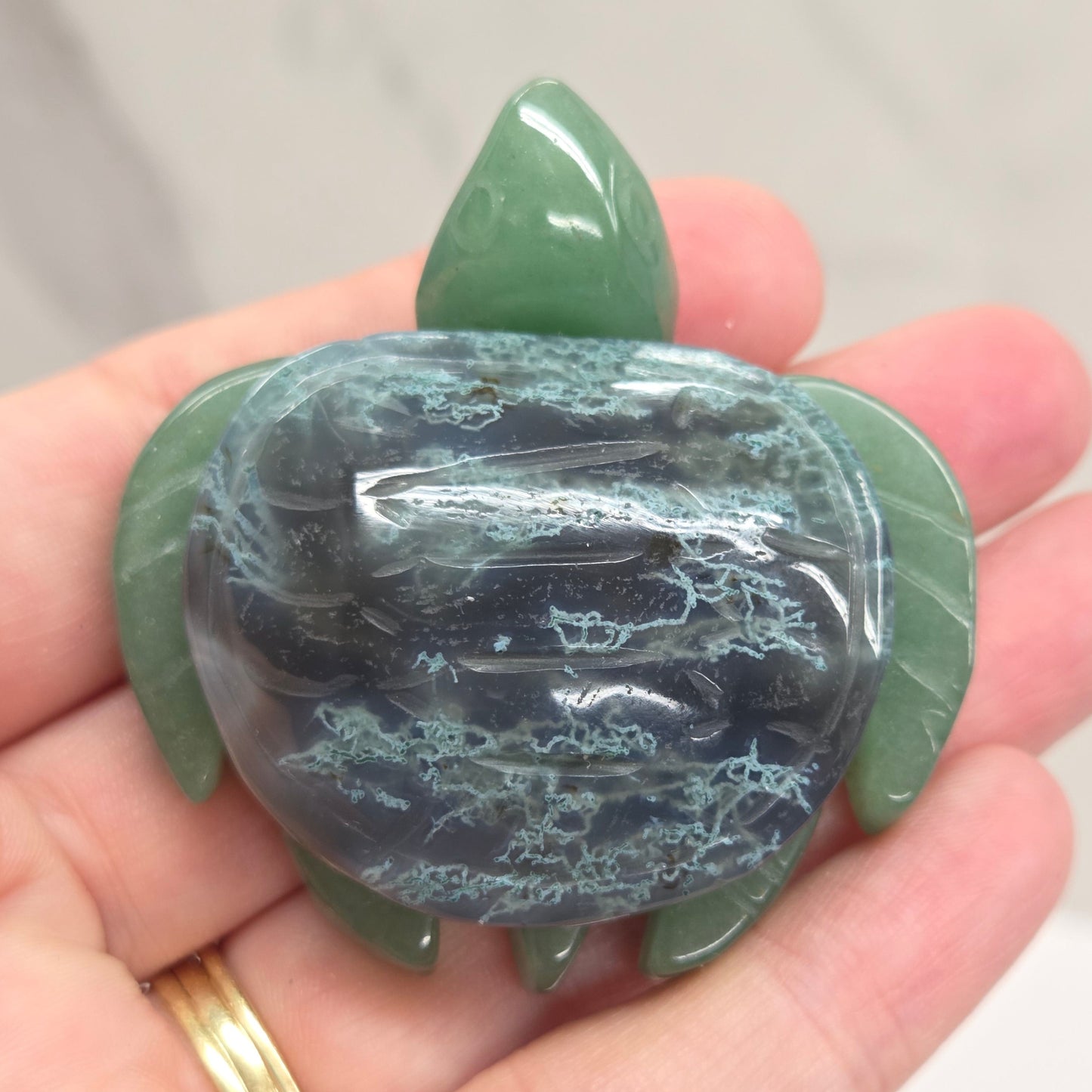 Hand holding a Jade turtle with a Moss Agate shell against a neutral background
