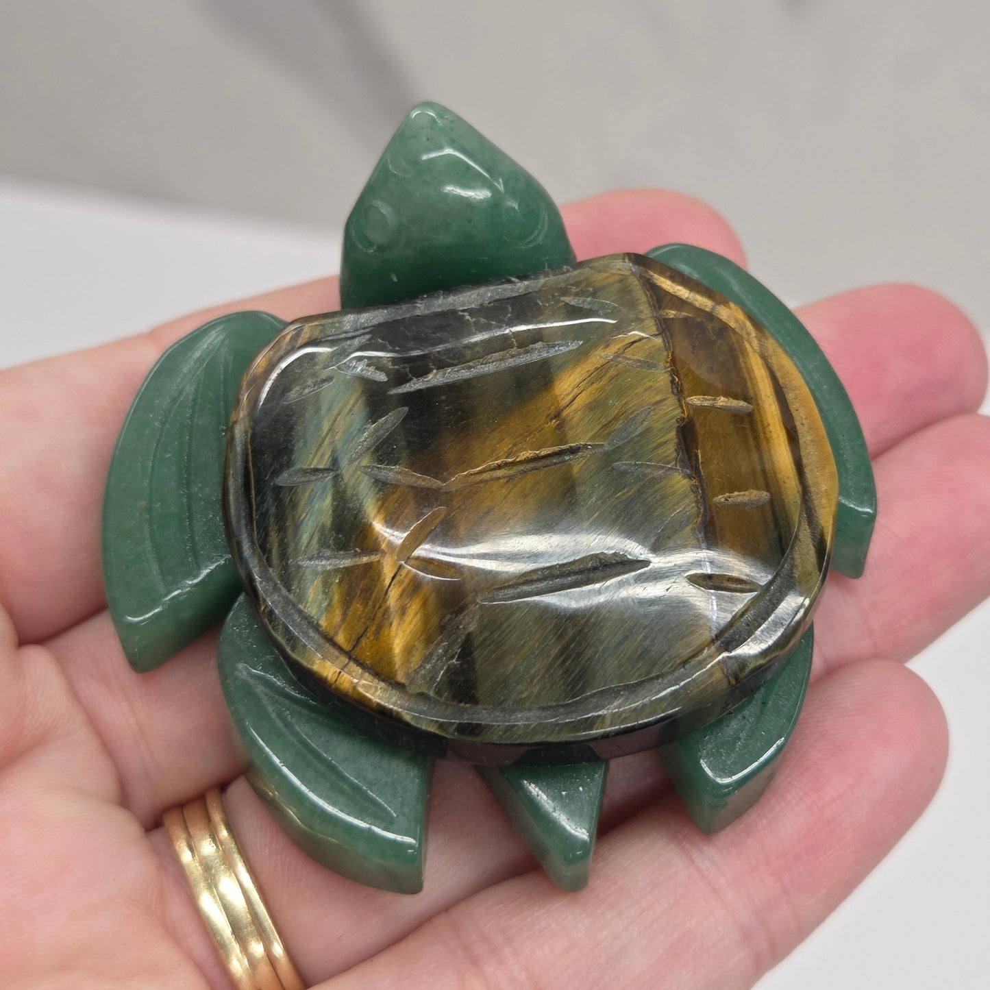 Hand holding a Jade turtle with a Blue Tigers Eye shell against a neutral background