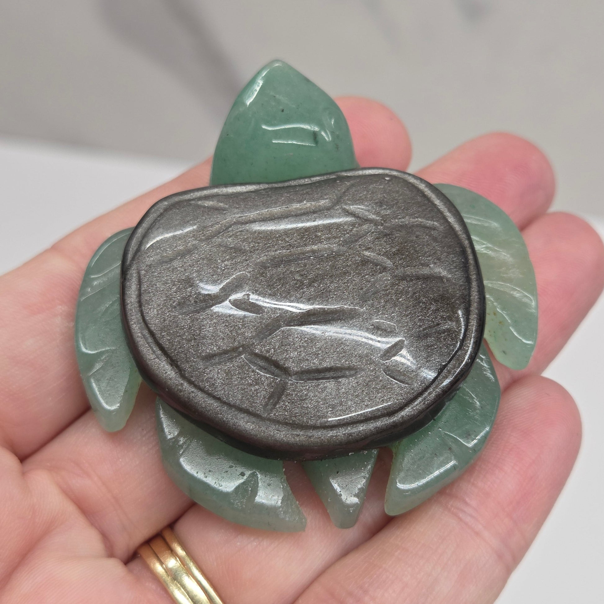 Hand holding a Jade turtle with a Silver Sheen Obsidian shell against a neutral background