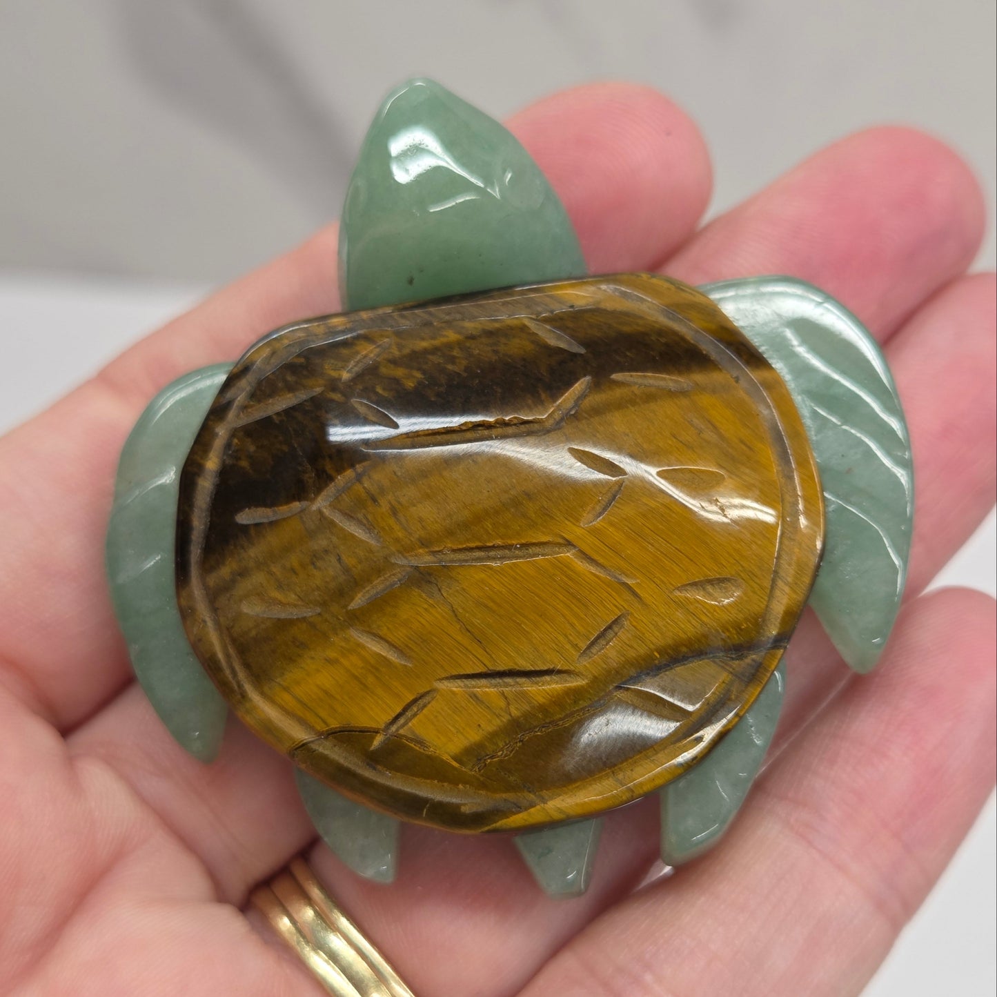Hand holding a Jade turtle with a Tigers Eye shell against a neutral background