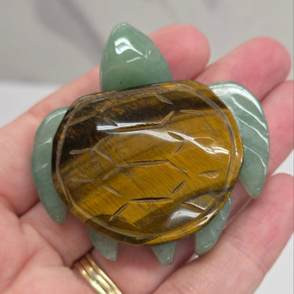 Hand holding a Jade turtle with a Tigers Eye shell against a neutral background