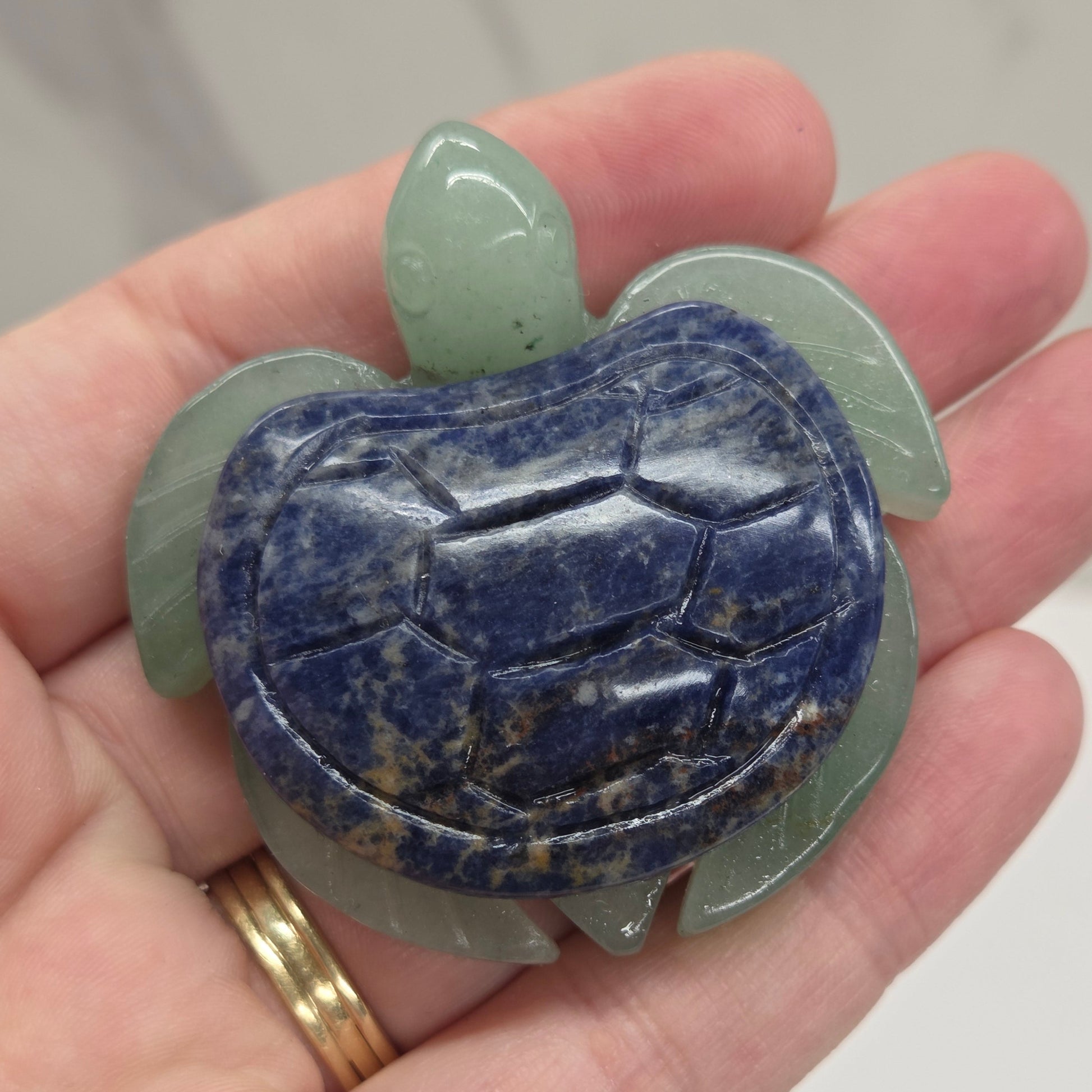 Hand holding a Jade turtle with a Sodalite shell against a neutral background