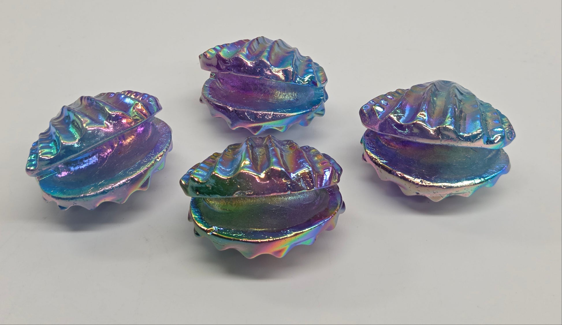 Four iridescent crystal clam-shaped objects on a gray background