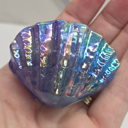 Hand holding a blue and purple iridescent crystal clam carving against a neutral background
