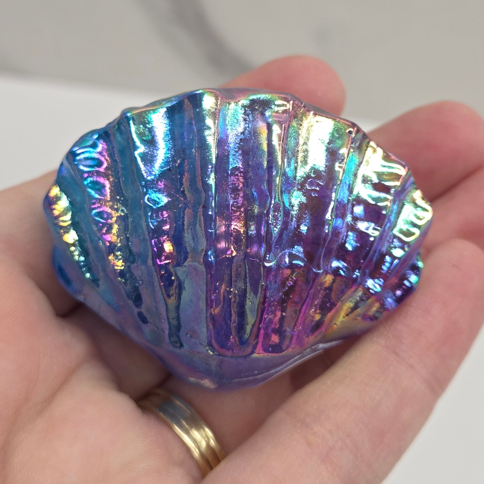 Hand holding a blue and purple iridescent crystal clam carving against a neutral background