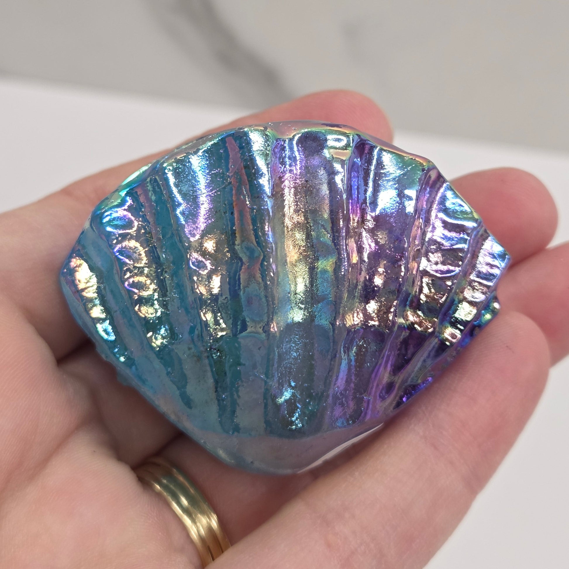 Hand holding a blue and purple iridescent crystal clam carving against a neutral background