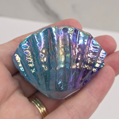 Hand holding a blue and purple iridescent crystal clam carving against a neutral background