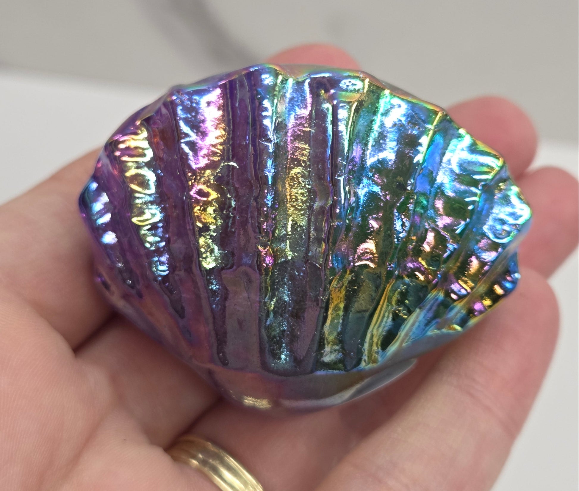 Hand holding a blue and purple iridescent crystal clam carving against a neutral background