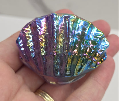 Hand holding a blue and purple iridescent crystal clam carving against a neutral background