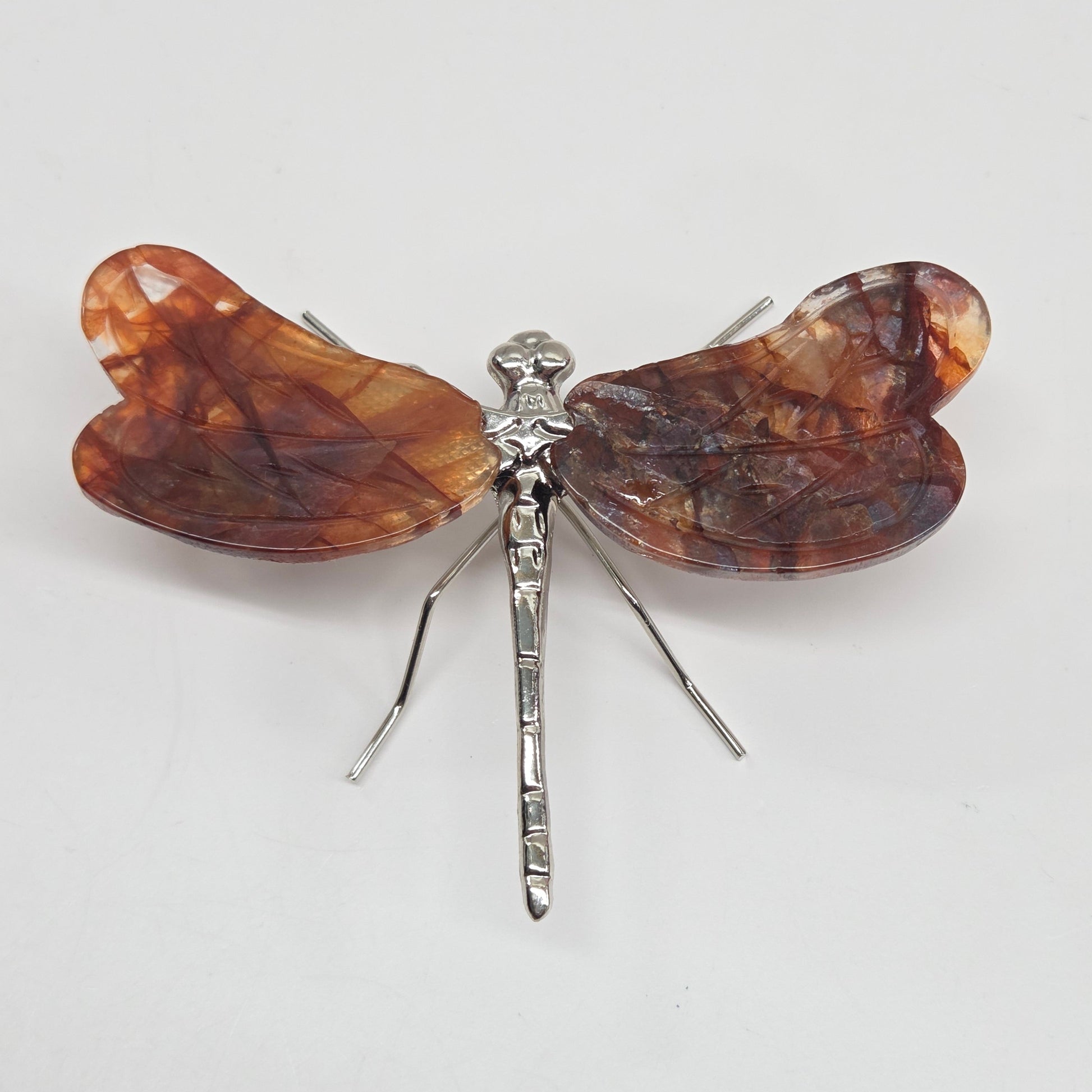 Dragonfly shaped carving with Fire Quartz crystal wings and a silver body on a white background